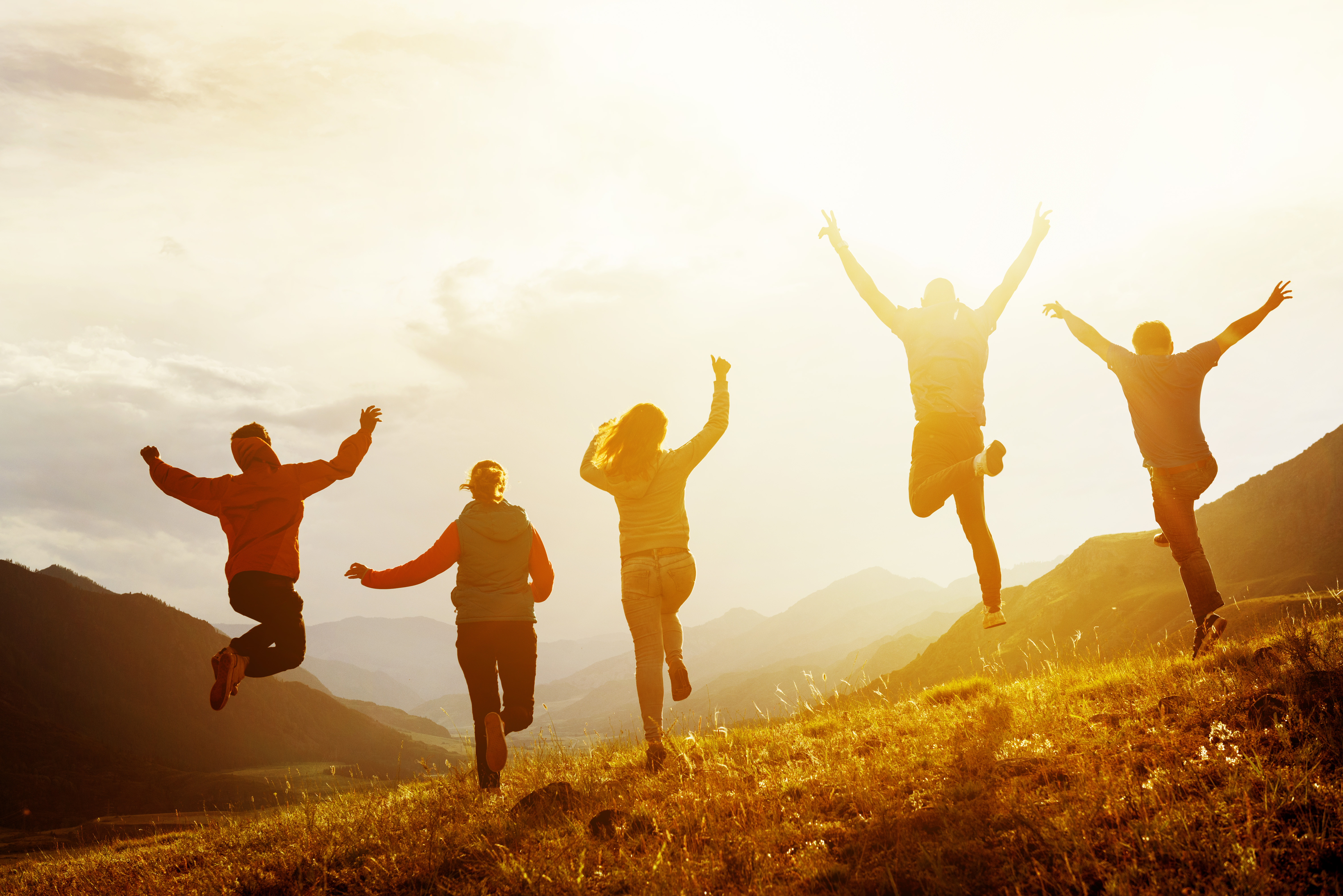 Group of five happy friends is running and jumping in sunset light on background of mountains. Happiness and friendship concept